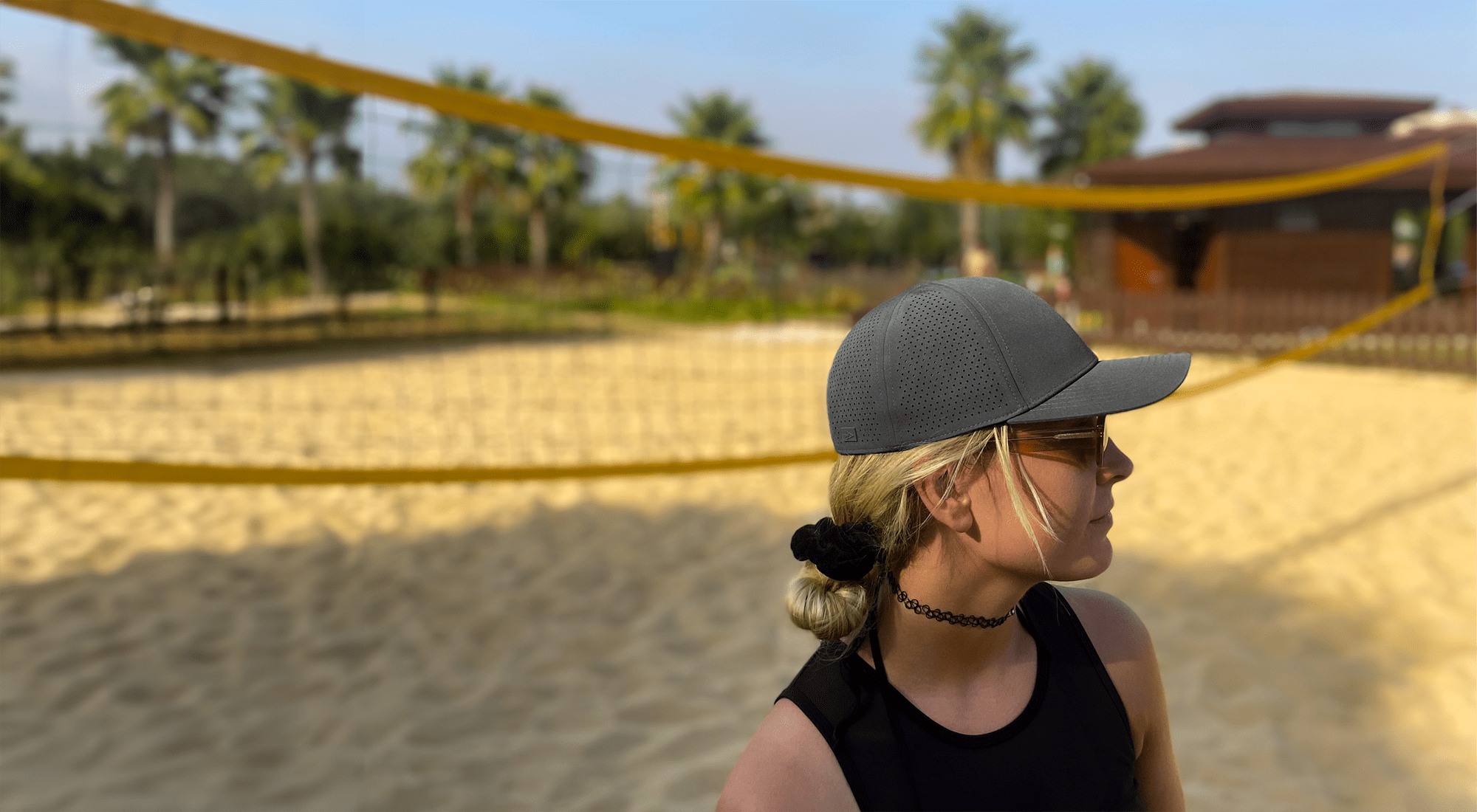 Frau mit apol Cap steht vor Beachvolleyballnetz in Sand