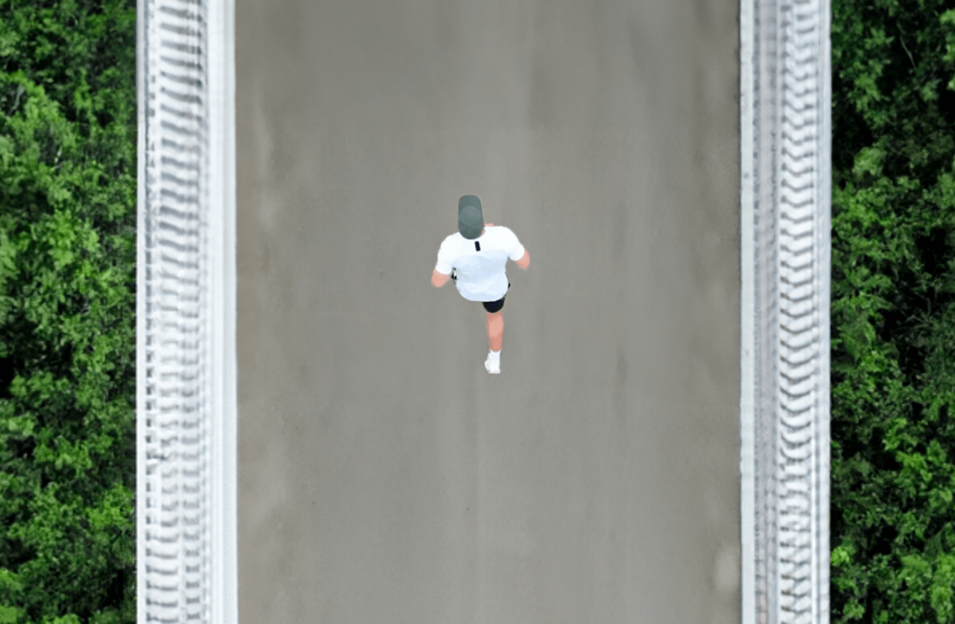 Mann aus vogelperspektive mit grüner apol Cap joggt über Brücke