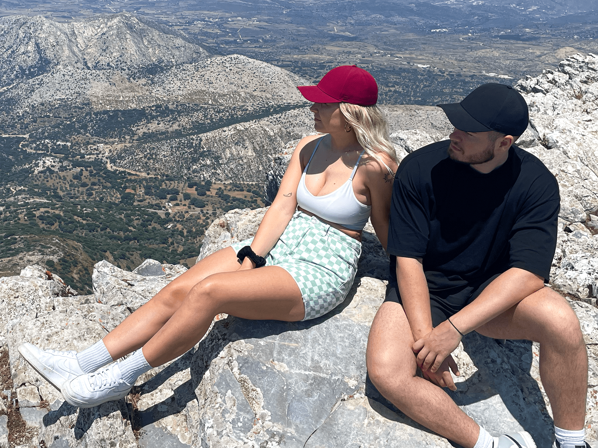 Mann und Frau mit apol Cap sitzen auf Berggipfel mit Bergpanorama im Hintergrund